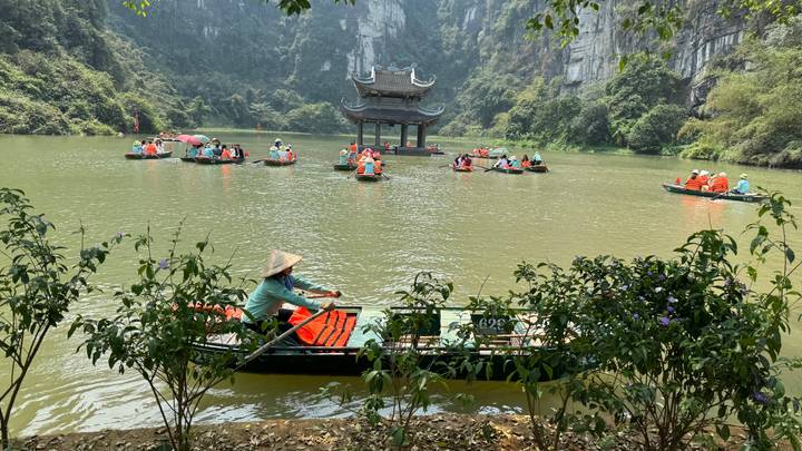 Dozens of visitors in rowboats paddling across a jade-green lagoon toward a pagoda in Ninh Binh.