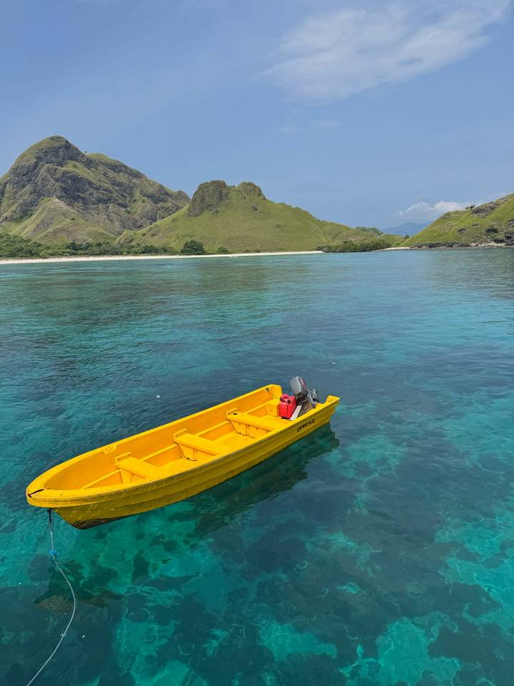 Bright yellow dinghy floating on crystal-clear turquoise water off a lush green island.