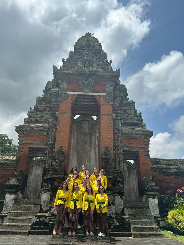 Travel group stands at a traditional red-brick Balinese temple gate under a cloudy sky.