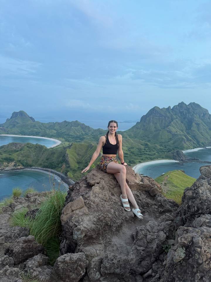 Woman sitting on a rocky summit overlooking the curved bays and green ridges of Padar Island.