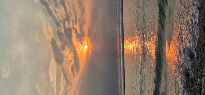 Orange sun setting over gentle ocean waves with golden reflection on the water.