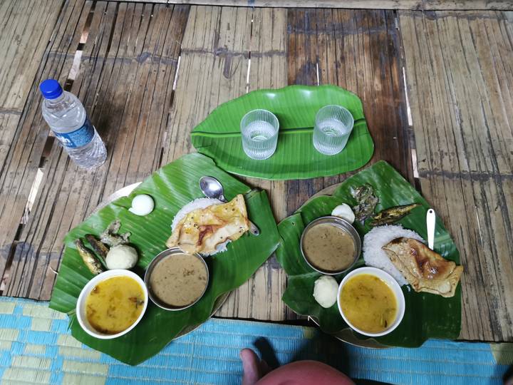 Traditional Assamese meal served on banana leaves with rice, curry, dal and accompaniments laid on a bamboo table.