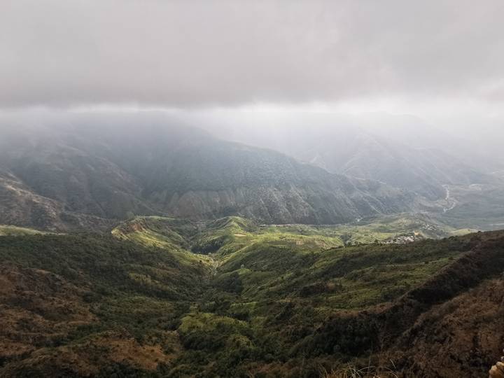 Misty mountain valley with dramatic layers of green ridges illuminated by shafts of sunlight through clouds.