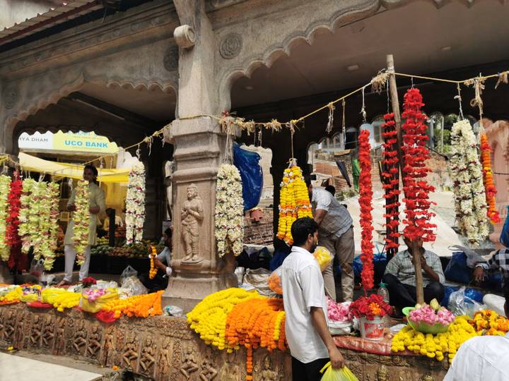 Busy flower market stall draped with colorful garlands and marigolds while vendors arrange blooms.