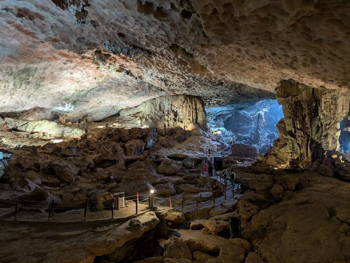 Illuminated interior of a vast limestone cave with walkways and dramatic stalactite formations.