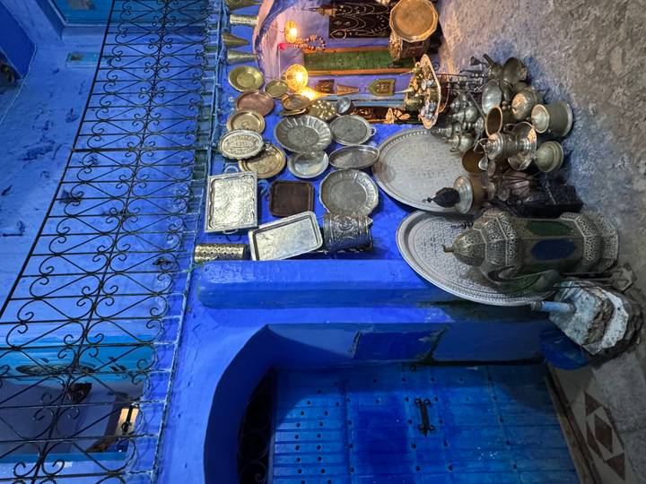 Deep blue alley in Chefchaouen lined with ornate metal trays and traditional brassware.