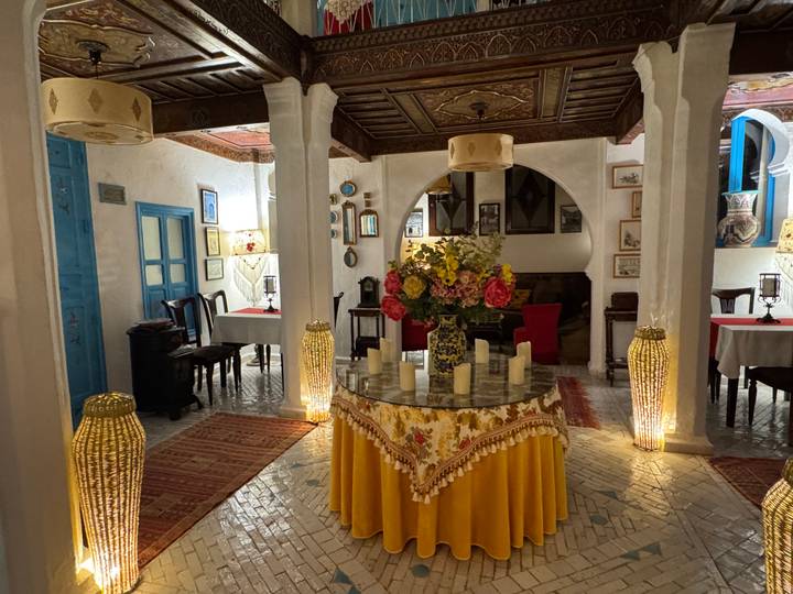 Cozy riad dining room with flower arrangement, candles and Moroccan decor softly lit.