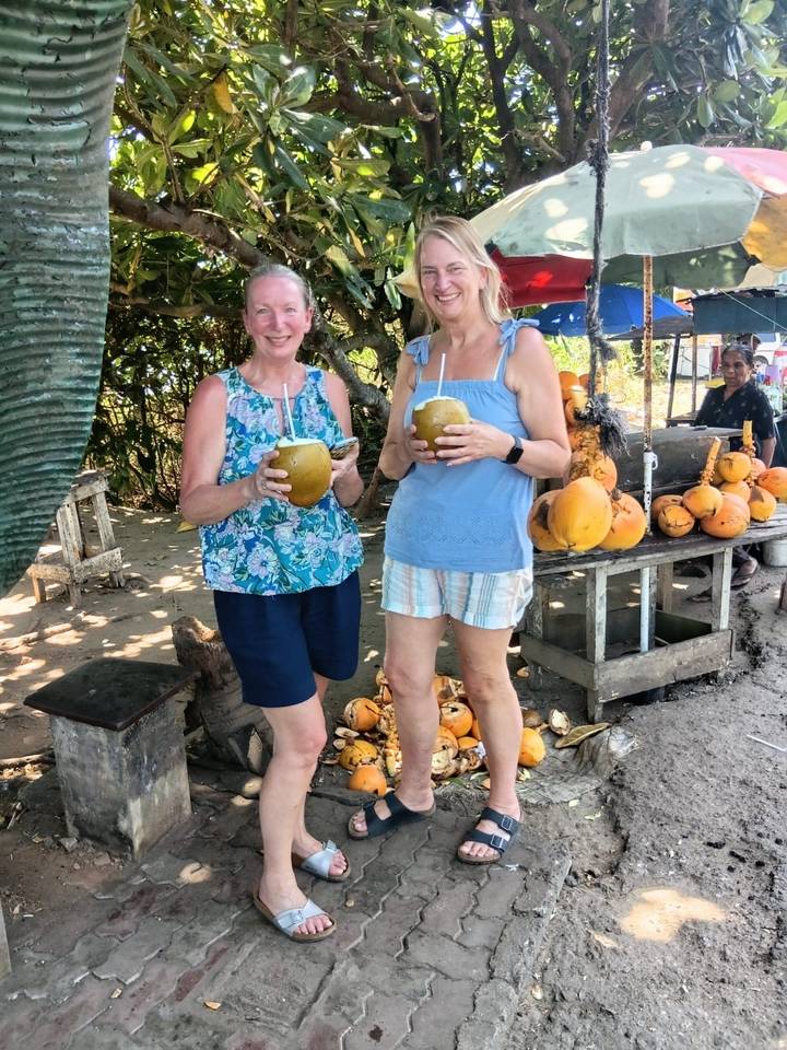 Travelers smile while drinking fresh king coconuts at a roadside fruit stall in Sri Lanka.