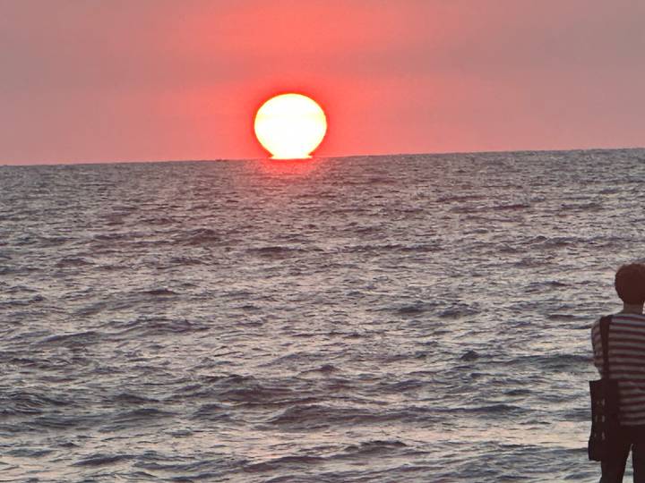 Brilliant orange sun sets into the Indian Ocean while a lone observer watches from shore.