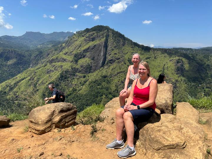Travelers rest on rocky viewpoint overlooking the lush peaks near Ella, Sri Lanka.
