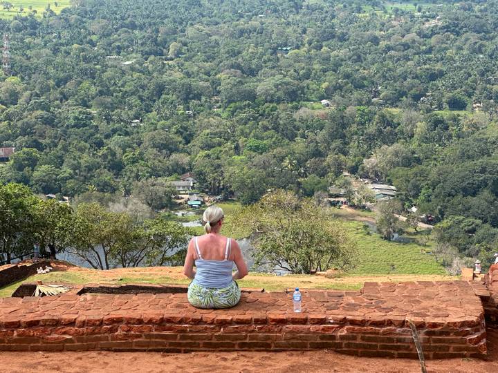 Woman meditates on a weathered brick ledge high above Sri Lanka’s lush plains at Sigiriya.