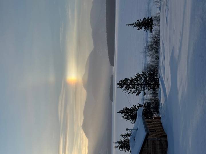 Winter lake with sun dog light phenomenon above distant snowy mountains