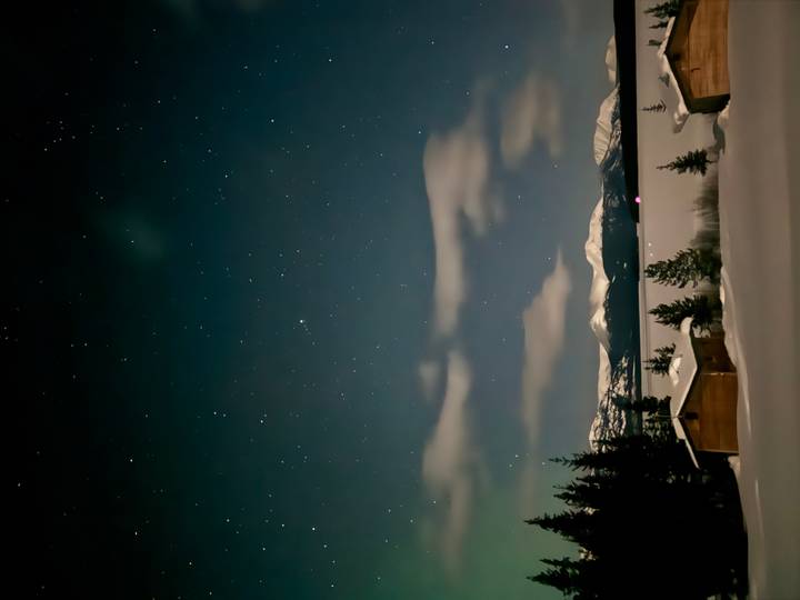 Starry night sky above snowy lake and distant mountain range with cabins