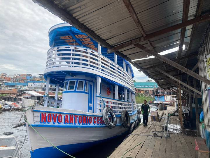 Traditional blue and white riverboat moored at rustic Amazon dock with local man nearby