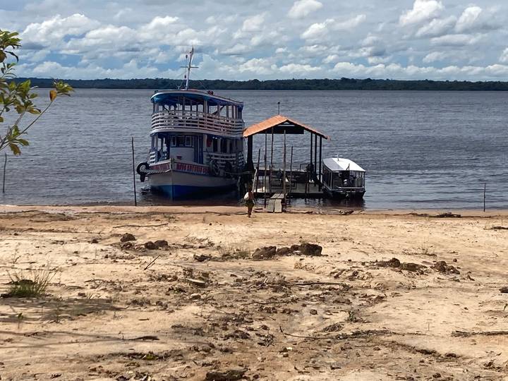 Riverboat anchored at sandy Amazon shore with wooden jetty and vast river view