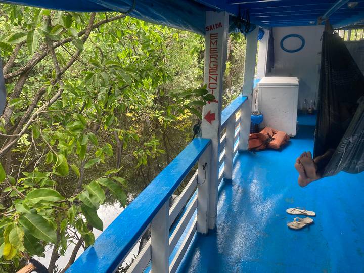Feet in hammock on blue-decked riverboat surrounded by lush flooded forest