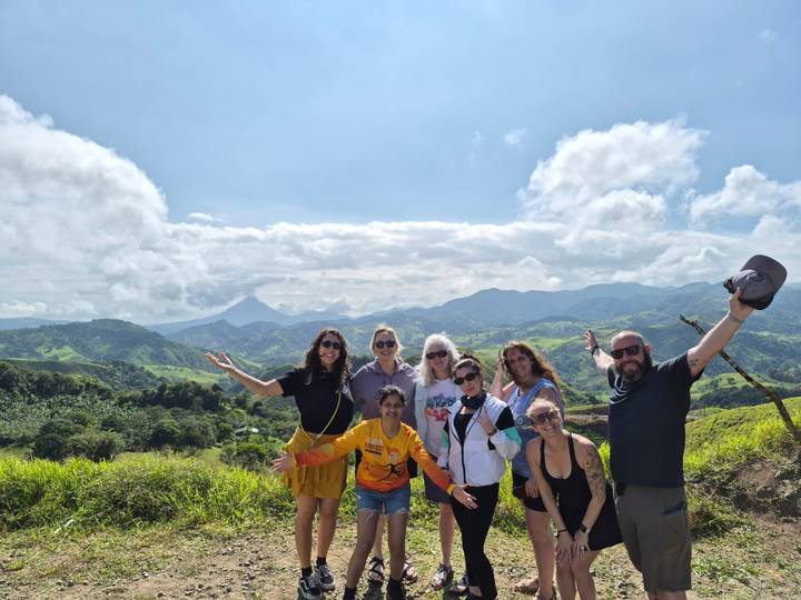 Smiling tour group posing on lush green hilltop with volcanic mountains in background