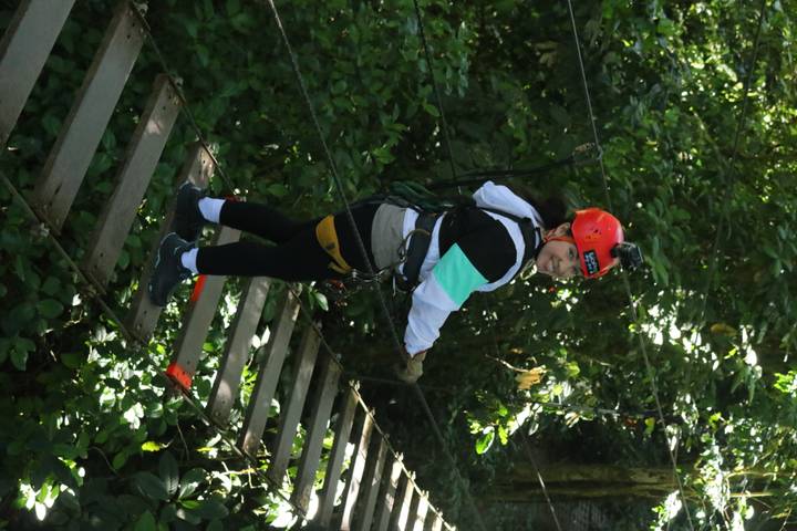 Participant smiling on wooden suspension bridge in rainforest wearing harness and helmet