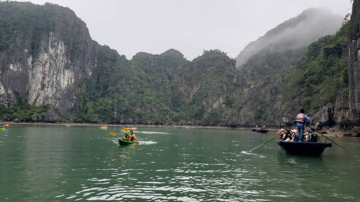 Kayakers paddling emerald waters beneath towering limestone cliffs in misty Ha Long Bay