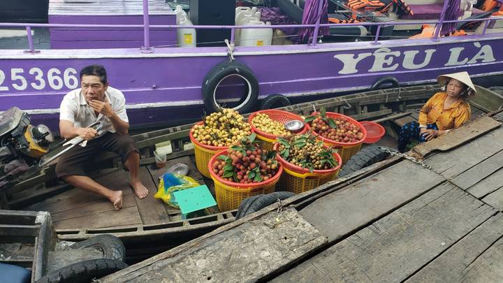 Vendors on a wooden boat selling colourful tropical fruit baskets at a floating market