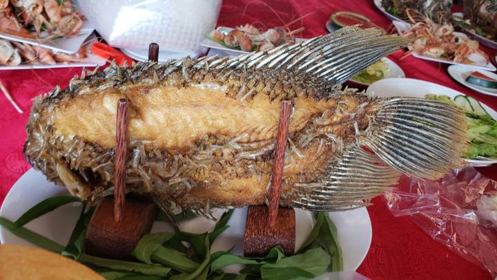 Whole fried fish on wooden skewers served on greens amid an array of seafood dishes
