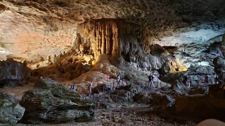 Vast illuminated limestone cave chamber with visitors walking along a raised boardwalk