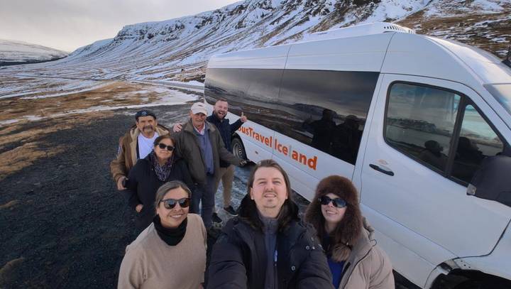 Group selfie beside a tour van parked in a snowy Icelandic valley.