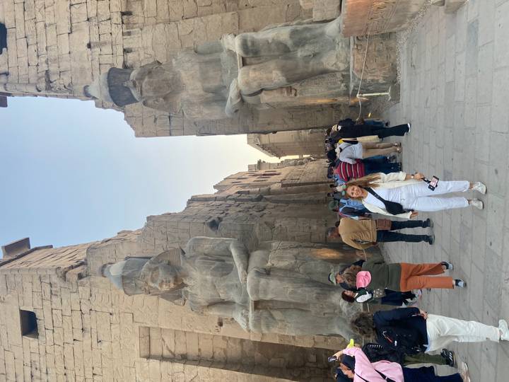 Visitor poses between colossal seated statues at the entrance of Luxor Temple.