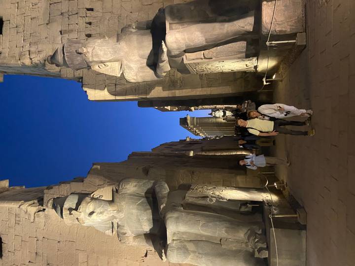 Visitors walk a night-lit avenue of statues at Luxor Temple under a deep blue sky.