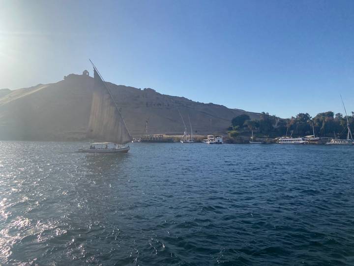 Traditional sailboat glides on the Nile with desert hills and ruins in the background.