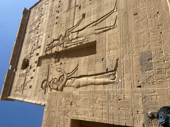 Detailed bas-reliefs on the sandstone walls of Philae Temple against a blue sky.