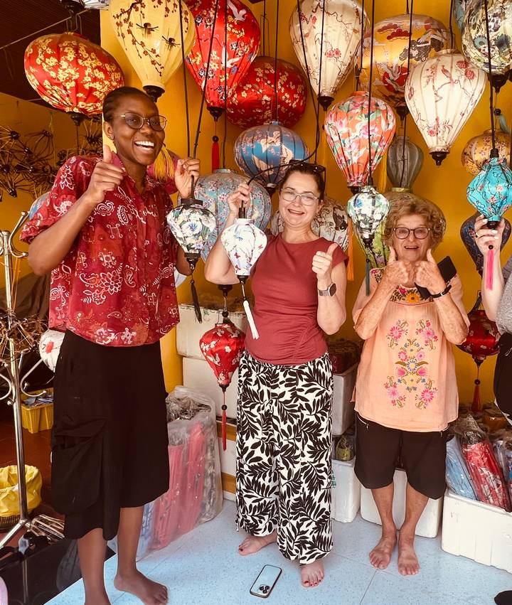 Travelers smile while crafting colorful lanterns inside a workshop.