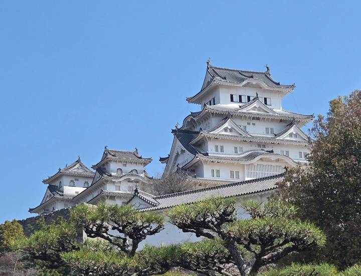 Immaculate white tiers and curved roofs of Himeji Castle rise majestically against a clear blue sky.
