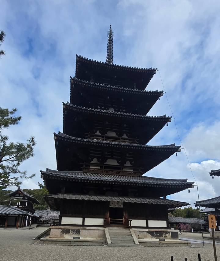 Silhouetted five-story pagoda stands tall against a partly cloudy sky in an ancient temple complex.