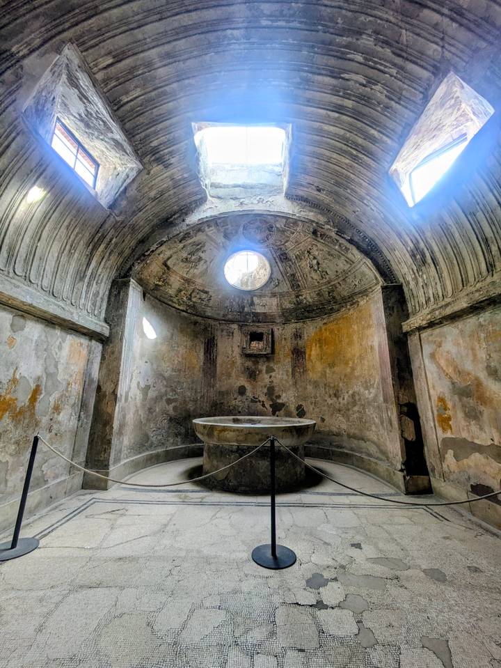 Ancient Roman bath chamber in Pompeii with circular basin and weathered frescoed dome ceiling.