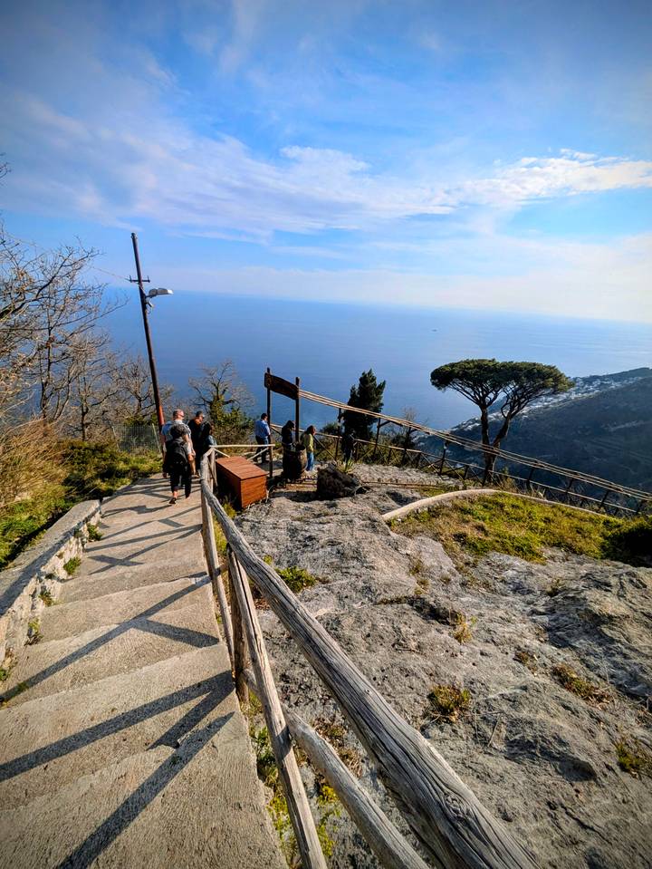 Hikers pause at a scenic lookout on a rocky trail high above the blue Mediterranean Sea.