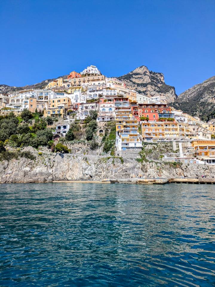Iconic colorful houses of Positano cascade down steep cliffs to the emerald sea viewed from a boat.