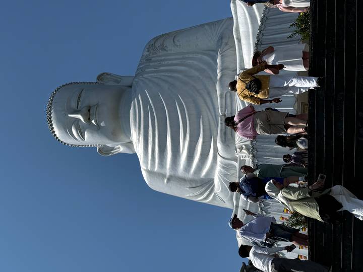 Massive white Buddha statue towers above visitors climbing the steps at Ba Na Hills under clear skies.
