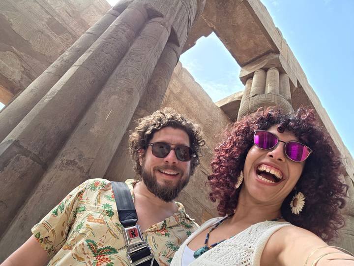 Smiling travellers take a selfie beneath towering sandstone columns and blue sky in an ancient Egyptian temple.
