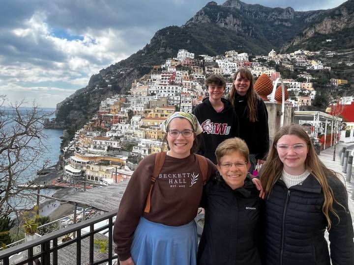 Group of travellers smiling with colorful Positano terraces cascading down the cliff behind
