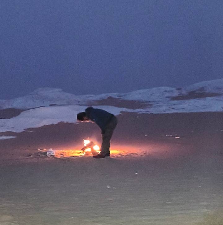 Traveler bending over a small campfire in the desert at dusk