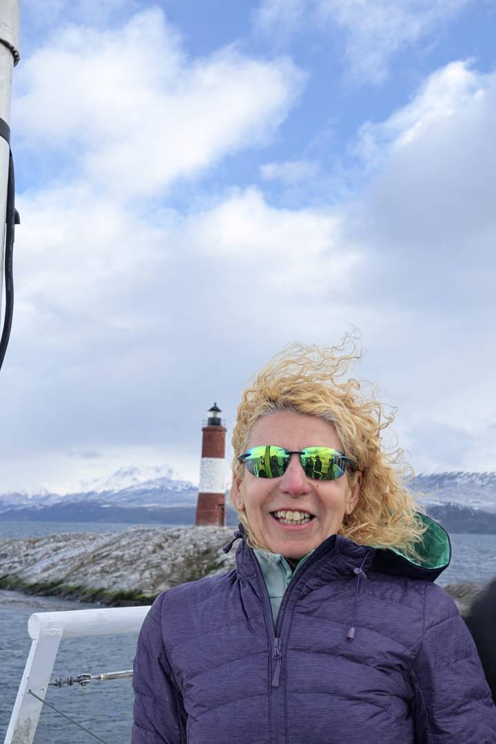 Close-up of a smiling traveler wearing mirrored sunglasses with the Les Éclaireurs lighthouse blurred in the background.