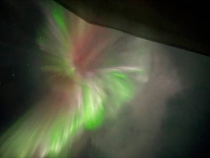 Blurred, abstract view of aurora lights in green and pink streaks against a cloudy night sky.
