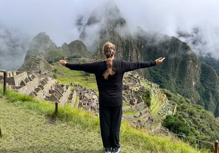 Back-view of a traveller with arms outstretched overlooking the misty terraces of Machu Picchu.