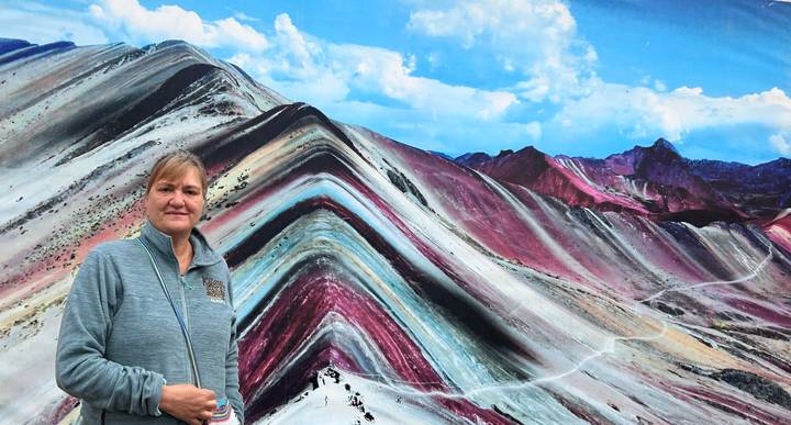 Traveller poses before a colourful panoramic mural depicting Peru’s Rainbow Mountain stripes.