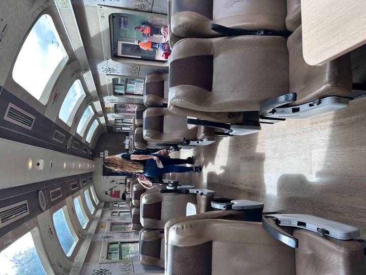 Interior of a scenic train carriage with large windows and a few passengers finding their seats.