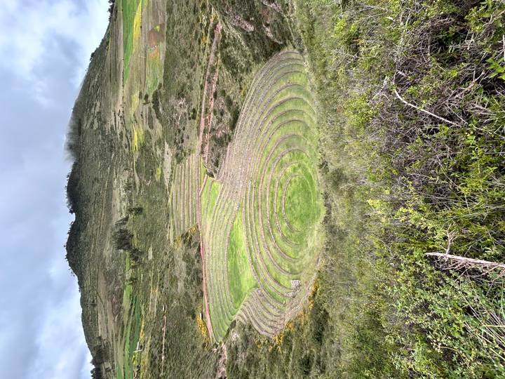 Wide view of the circular agricultural terraces of Moray set into a green hillside under a moody sky.