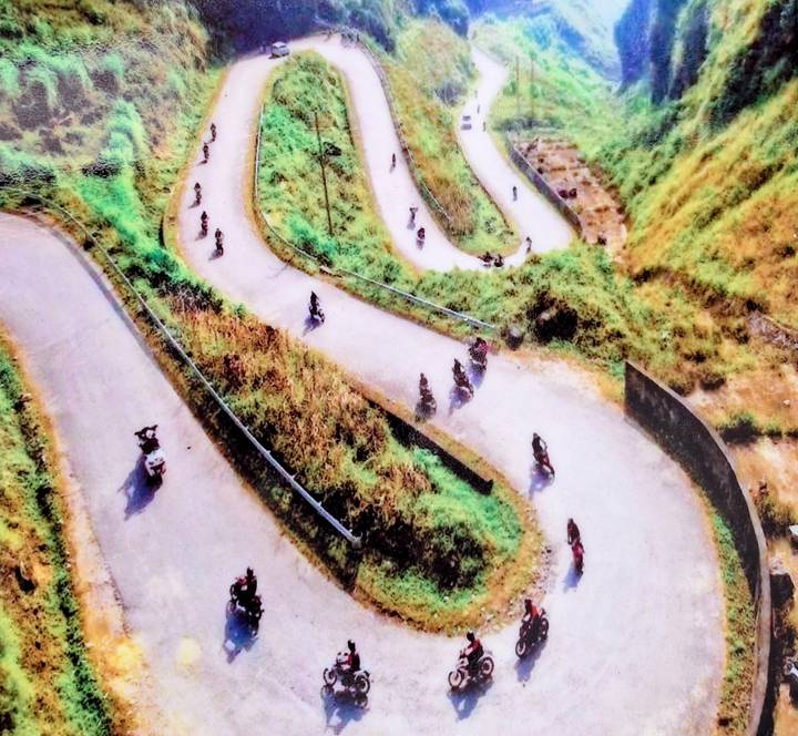 Blurry aerial image of winding mountain road filled with motorbikes carving sharp switchbacks.