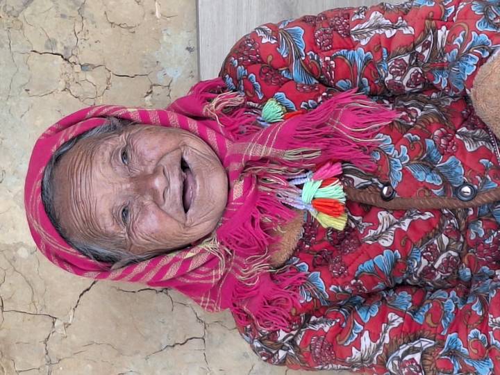 Close-up portrait of an elderly woman smiling broadly, wearing a bright patterned scarf and dress.