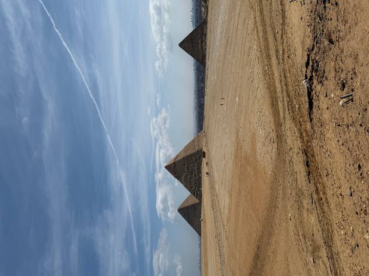 Wide desert vista with the three main pyramids of Giza rising from the sands beneath streaked blue sky.